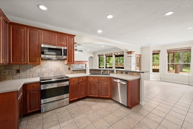 10 Hollow Glen Ln, Tomball, TX 77375 - kitchen with stainless steel appliances, a peninsula, a sink, light tile patterned floors, and crown molding