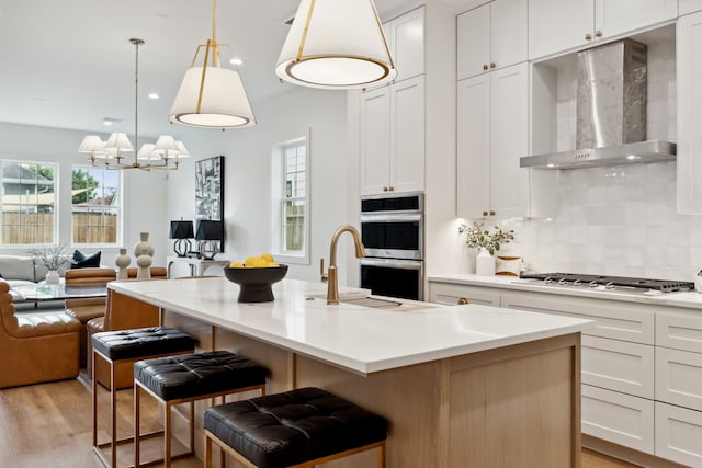 kitchen featuring wall chimney exhaust hood, stainless steel appliances, open floor plan, light wood-type flooring, and light countertops