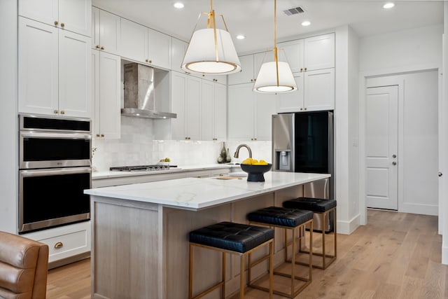 kitchen with wall chimney range hood, appliances with stainless steel finishes, light wood-style floors, a kitchen island, and recessed lighting