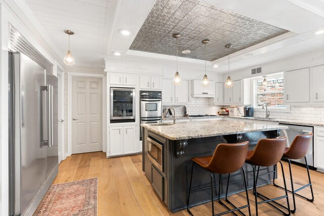 42 Cherry Hill Dr, Conroe, TX 77304 - kitchen with stainless steel appliances, a raised ceiling, white cabinets, a kitchen island with sink, and light wood-style flooring