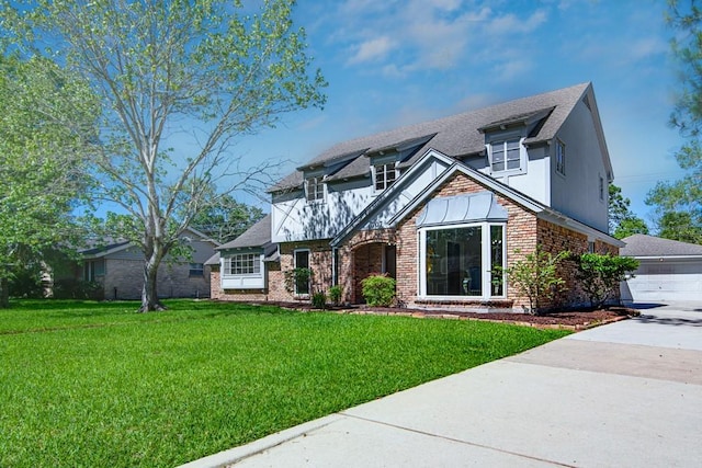 tudor-style house featuring roof with shingles, brick siding, a front lawn, and driveway