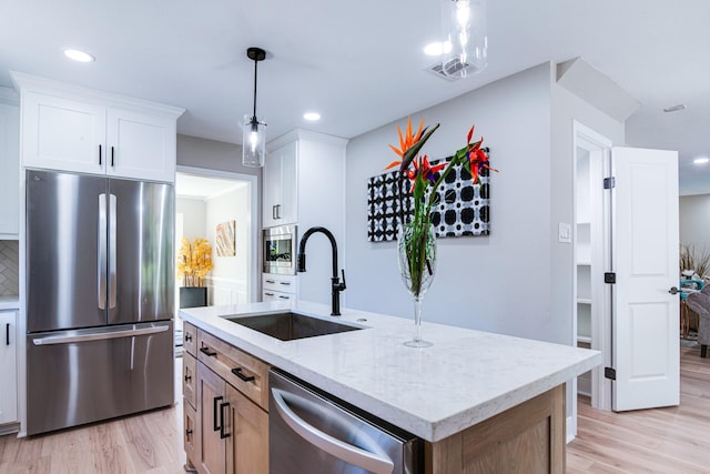 kitchen with stainless steel appliances, a sink, light wood finished floors, light stone countertops, and decorative light fixtures