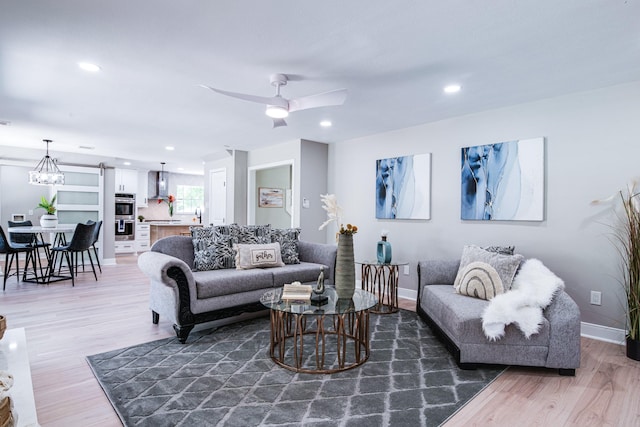 living room featuring light wood-type flooring, ceiling fan, baseboards, recessed lighting, and a chandelier