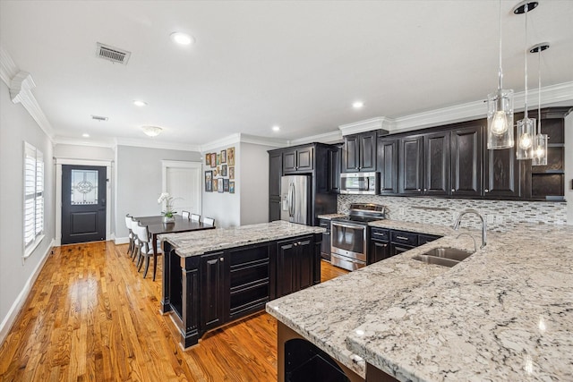 kitchen featuring appliances with stainless steel finishes, a sink, a kitchen island, backsplash, and dark cabinetry