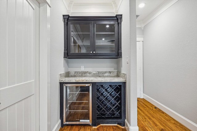 indoor dry bar with beverage cooler, crown molding, wood finished floors, and baseboards