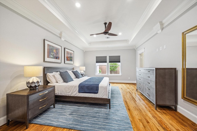 bedroom featuring a tray ceiling, crown molding, wood finished floors, baseboards, and recessed lighting