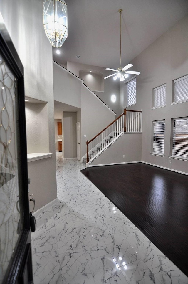 foyer entrance featuring stairway, baseboards, ceiling fan, a high ceiling, and marble finish floors