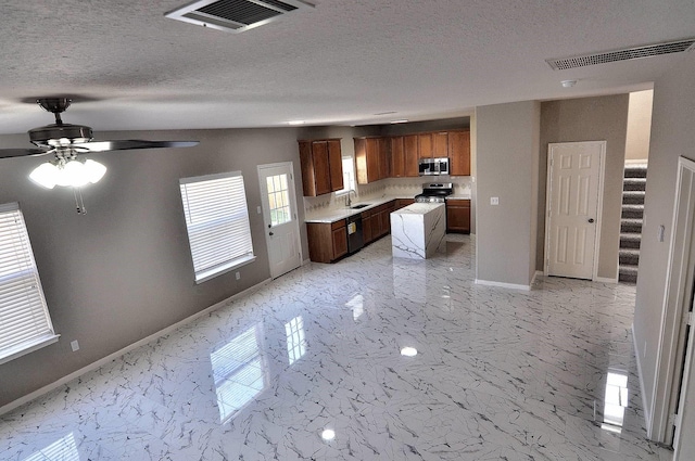 kitchen with appliances with stainless steel finishes, a sink, light countertops, baseboards, and light marble finish flooring