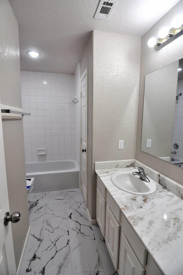 bathroom with a textured ceiling, bathing tub / shower combination, vanity, marble finish floors, and a textured wall