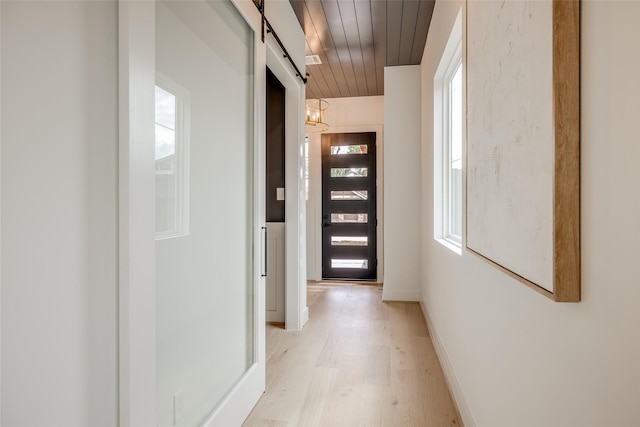 hall with wooden ceiling, light wood-type flooring, baseboards, a barn door, and a chandelier