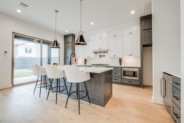 kitchen featuring stainless steel microwave, under cabinet range hood, light countertops, tasteful backsplash, and light wood-style floors