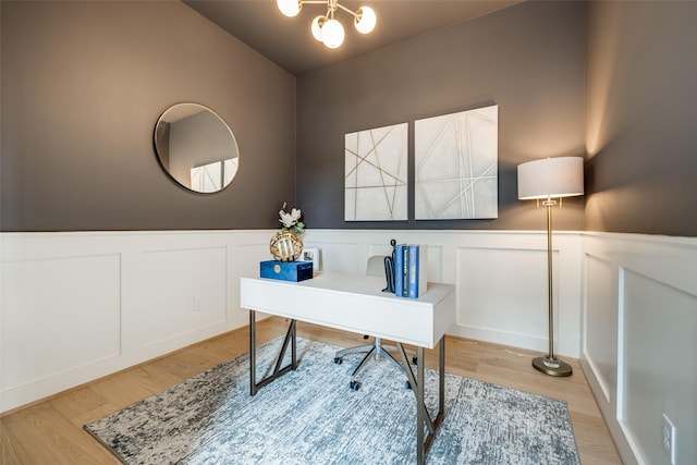 office space featuring wainscoting, a decorative wall, light wood-style floors, and a chandelier