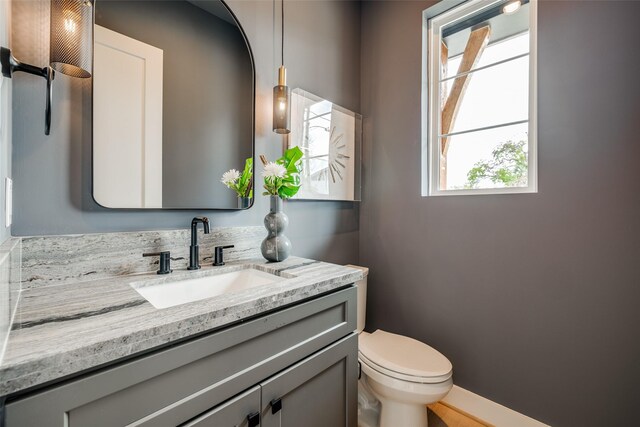 half bathroom with healthy amount of natural light, toilet, vanity, and baseboards