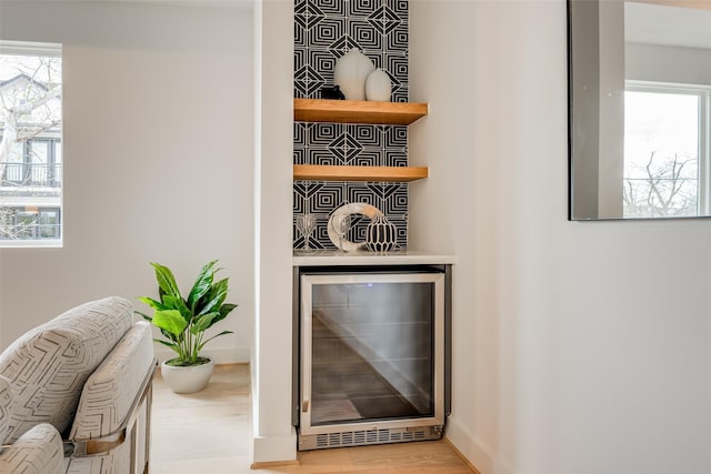 detailed view of beverage cooler, a bar, wood finished floors, and baseboards