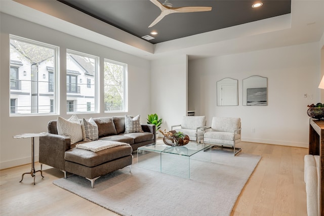 living room featuring a tray ceiling, light wood-style flooring, baseboards, ceiling fan, and recessed lighting