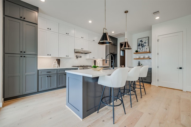 kitchen featuring under cabinet range hood, decorative backsplash, light wood-style flooring, light countertops, and recessed lighting