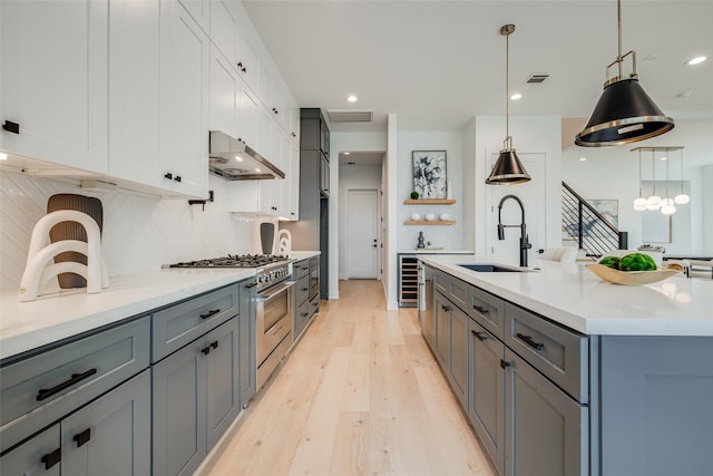 kitchen with a sink, stainless steel range, under cabinet range hood, light countertops, and recessed lighting