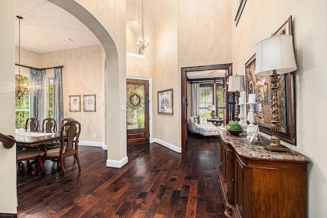 foyer entrance featuring a chandelier, dark wood-style floors, arched walkways, baseboards, and a towering ceiling