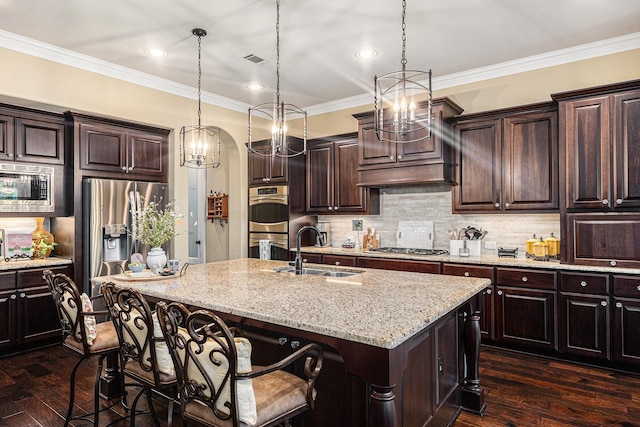 kitchen featuring a sink, appliances with stainless steel finishes, a kitchen bar, a kitchen island with sink, and light stone counters