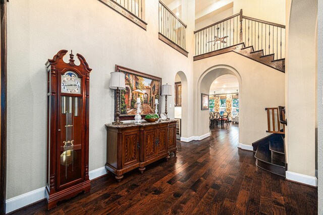 foyer entrance featuring arched walkways, dark wood-style flooring, stairs, baseboards, and a high ceiling