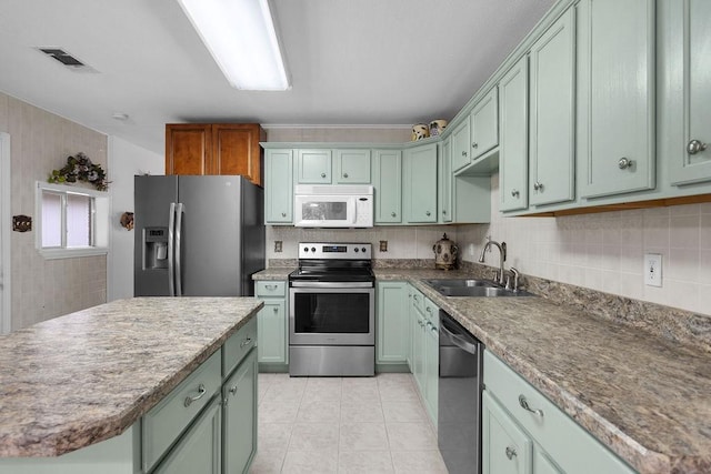 24930 Plantation Estates Ave, Porter, TX 77365 - kitchen with appliances with stainless steel finishes, a sink, green cabinetry, light tile patterned floors, and backsplash