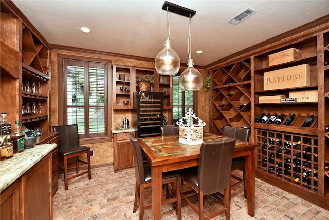 wine area with brick patterned flooring, a textured ceiling, and crown molding
