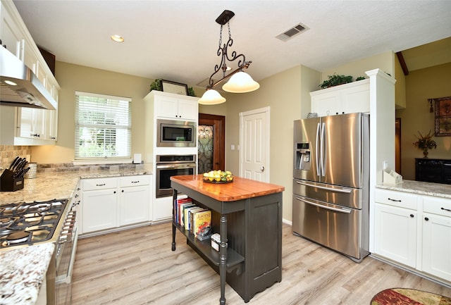 kitchen featuring stainless steel appliances, light wood-type flooring, butcher block counters, white cabinetry, and decorative light fixtures