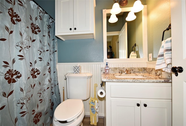 bathroom featuring wainscoting, vanity, toilet, curtained shower, and a decorative wall