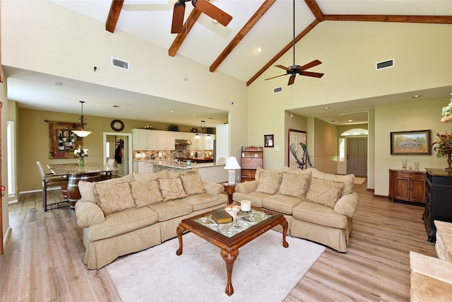 living room featuring a ceiling fan, high vaulted ceiling, light wood-style flooring, beamed ceiling, and baseboards