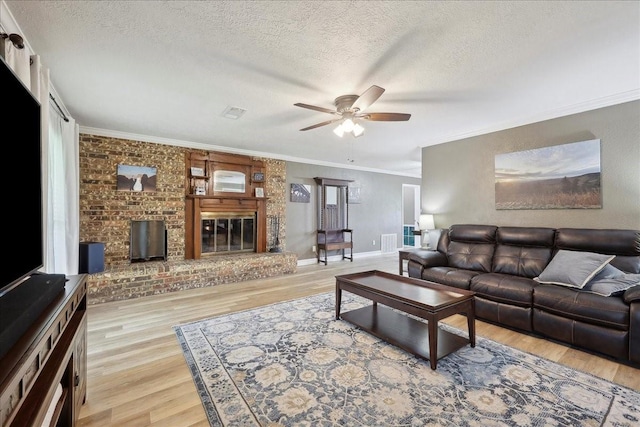 985 Sunnyside Dr, Bridge City, TX 77611 - living room with ceiling fan, a textured ceiling, a brick fireplace, light wood-style floors, and ornamental molding