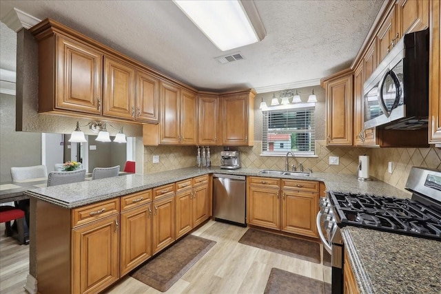 985 Sunnyside Dr, Bridge City, TX 77611 - kitchen featuring stainless steel appliances, a sink, light wood-style flooring, brown cabinetry, and a textured ceiling