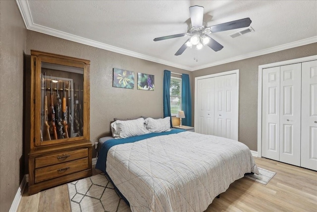 985 Sunnyside Dr, Bridge City, TX 77611 - bedroom featuring a textured wall, light wood-style flooring, multiple closets, ornamental molding, and baseboards