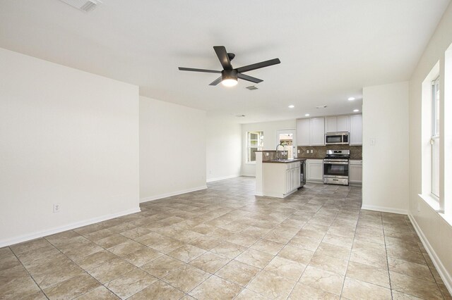 unfurnished living room with a ceiling fan, recessed lighting, a sink, baseboards, and light stone finish flooring