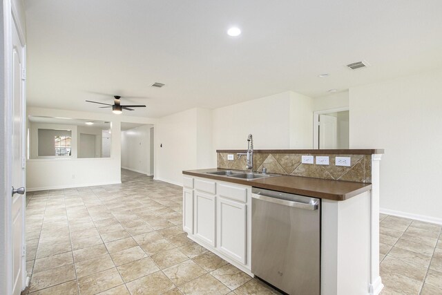 kitchen with stainless steel dishwasher, a sink, dark countertops, white cabinets, and decorative backsplash
