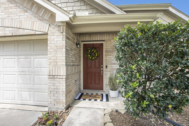 doorway to property featuring an attached garage and brick siding