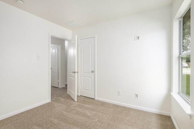 spare room featuring light colored carpet, baseboards, and plenty of natural light