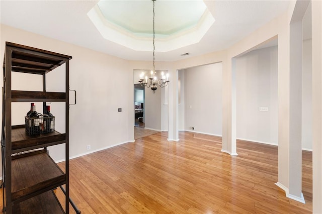 unfurnished dining area with a chandelier, light wood-type flooring, baseboards, and a tray ceiling