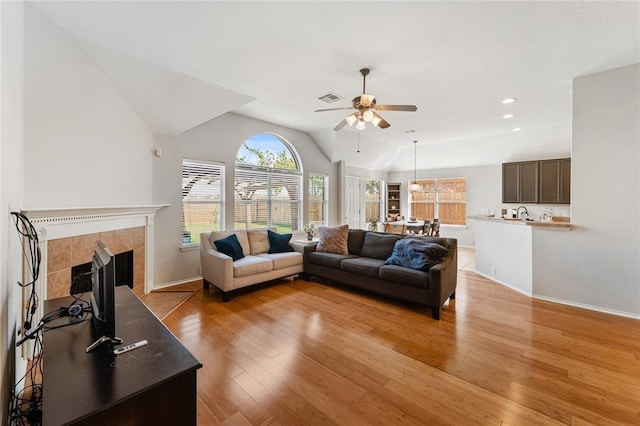 living area with a ceiling fan, light wood finished floors, vaulted ceiling, a tile fireplace, and recessed lighting