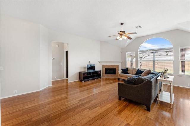 living room with a ceiling fan, light wood-type flooring, a tile fireplace, lofted ceiling, and baseboards