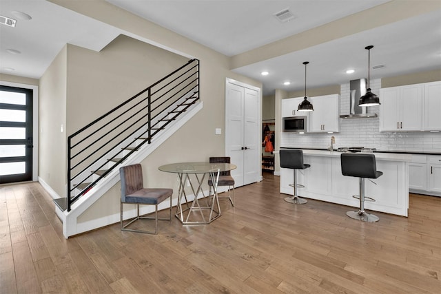 kitchen featuring wall chimney exhaust hood, stainless steel microwave, decorative backsplash, light wood-style floors, and white cabinets