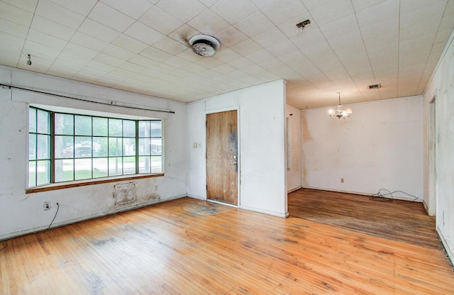 empty room with a chandelier, wood-type flooring, and a pendent fire sprinkler