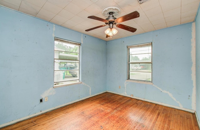 unfurnished room with healthy amount of natural light, wood-type flooring, a ceiling fan, and baseboards