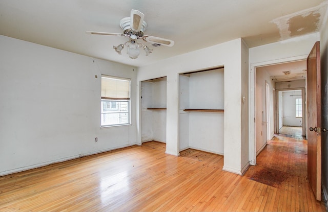 unfurnished bedroom featuring two closets, hardwood / wood-style floors, multiple windows, and baseboards