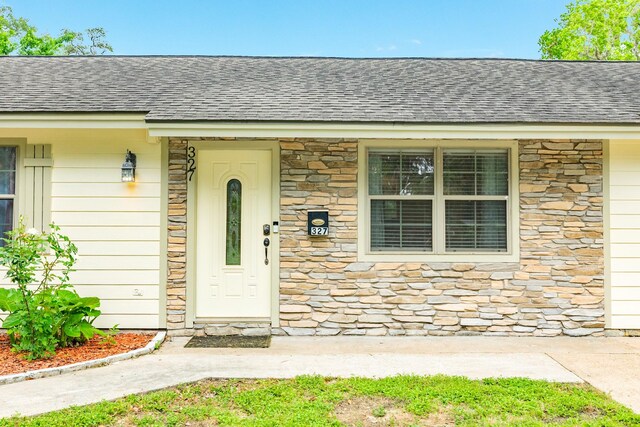 entrance to property featuring roof with shingles and stone siding