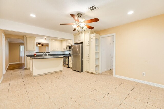 kitchen featuring stainless steel appliances, a ceiling fan, a sink, dark countertops, and cream cabinets