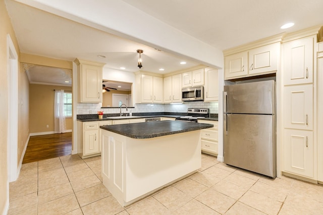 kitchen with stainless steel appliances, a sink, cream cabinetry, light tile patterned floors, and backsplash