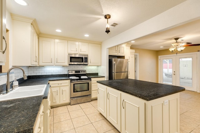 kitchen featuring appliances with stainless steel finishes, a sink, light tile patterned floors, backsplash, and a center island