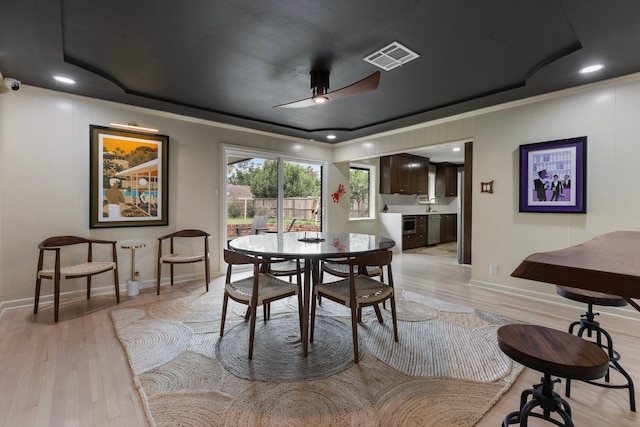 dining area featuring a tray ceiling, light wood-style flooring, baseboards, ceiling fan, and crown molding