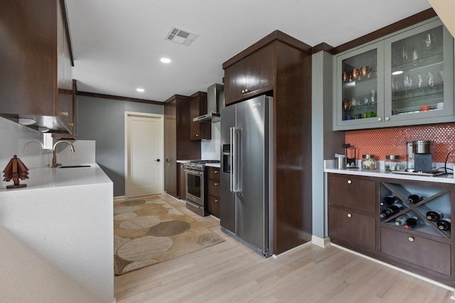 kitchen featuring premium appliances, wall chimney range hood, light wood-style floors, dark brown cabinetry, and recessed lighting