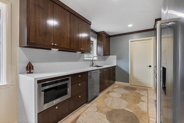 kitchen with stainless steel appliances, dark brown cabinets, light countertops, light wood-type flooring, and ornamental molding